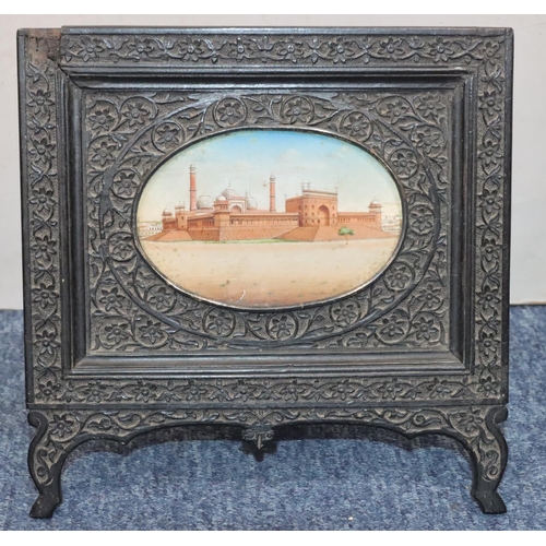 828 - An Eastern oval miniature depicting palace, in ebony frame with allover carved floral and leaf decor... 