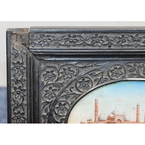 828 - An Eastern oval miniature depicting palace, in ebony frame with allover carved floral and leaf decor... 