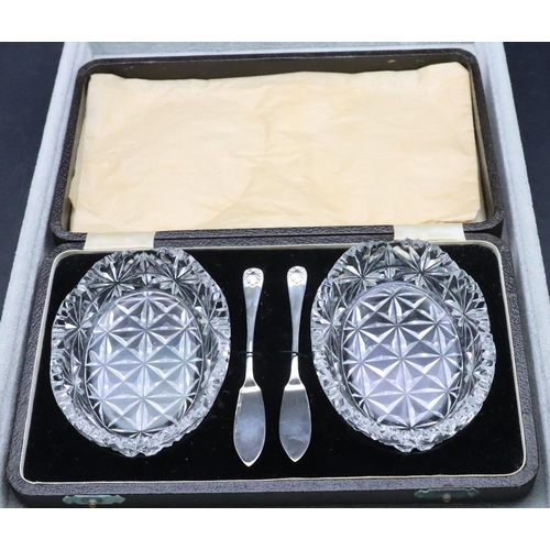 452 - A pair of cut glass oval butter dishes with a pair of Birmingham silver butter knives in fitted blac... 