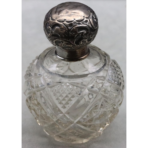 484 - A cut glass round bulbous shaped scent bottle with silver top embossed with leaf and scroll decorati... 