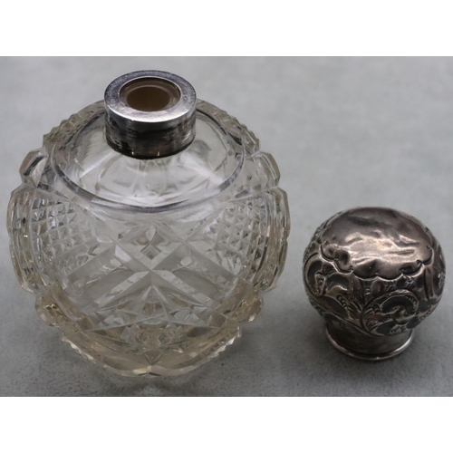 484 - A cut glass round bulbous shaped scent bottle with silver top embossed with leaf and scroll decorati... 