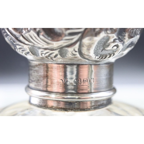 484 - A cut glass round bulbous shaped scent bottle with silver top embossed with leaf and scroll decorati... 