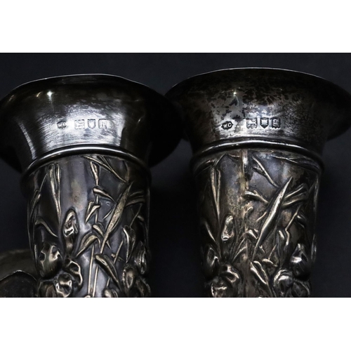 493 - A pair of London silver round trumpet shaped spill vases with embossed floral and leaf decoration on... 