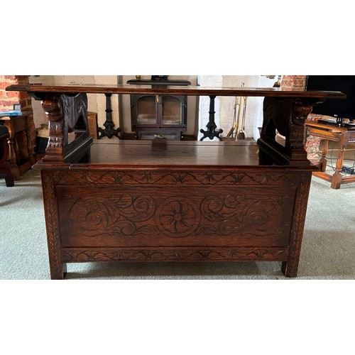 9227 - An oak monk's bench with carved decoration and ornate arms in the style of lions, on square feet.  C... 