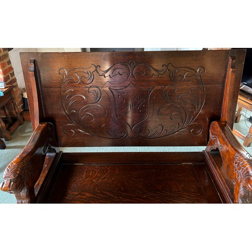 9227 - An oak monk's bench with carved decoration and ornate arms in the style of lions, on square feet.  C... 