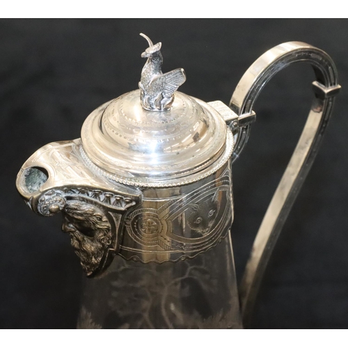 128 - A silver plated and engraved glass round bulbous shaped claret jug with mask head spout and hinged l... 