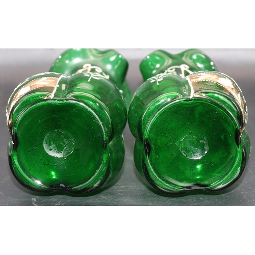 34 - A pair of green glass bulbous thin necked jugs with crinkle rims and raised floral, leaf and scroll ... 