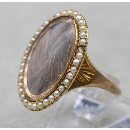 703 - An 18th Century Mourning gold ring with oval top, inset with plaited hair surrounded by half pearls ... 