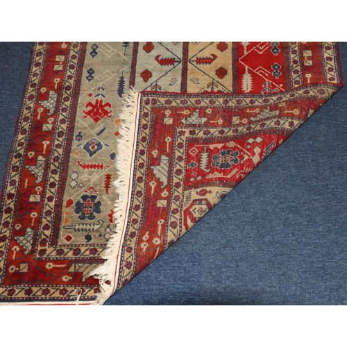 828 - A Persian rug on red and blue ground with 4 centre strips with hook and floral design, 131cm x 83cm