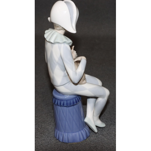 131 - A Lladro figure of a seated young boy dressed as a jester holding a cat, 23cm high