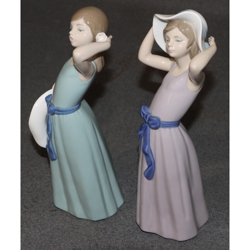 133 - 2 Lladro figures of standing young ladies holding hats wearing purple and green dresses, largest 26c... 