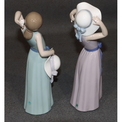 133 - 2 Lladro figures of standing young ladies holding hats wearing purple and green dresses, largest 26c... 