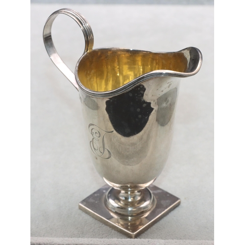 353 - A George V silver helmet shaped cream jug with scroll handle and reeded rim on square base, London 1... 