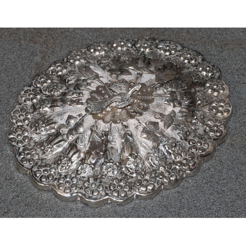 491 - An Eastern silver coloured metal oval scallop shaped hand mirror with raised and embossed bird, flor... 