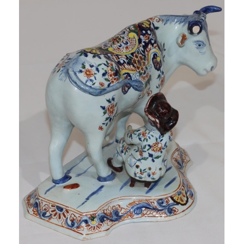 88 - A Dutch Delft group of seated figure milking a cow on white and blue ground with multi-coloured flor... 