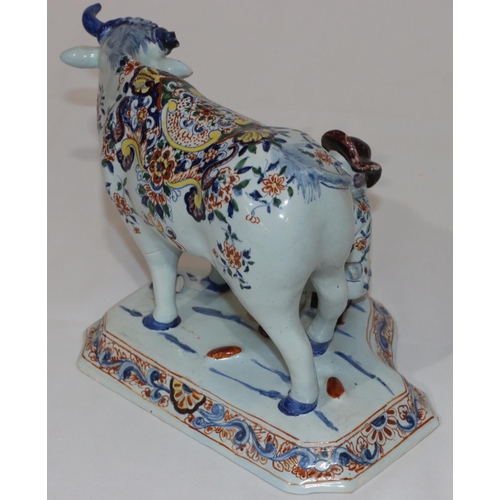 88 - A Dutch Delft group of seated figure milking a cow on white and blue ground with multi-coloured flor... 