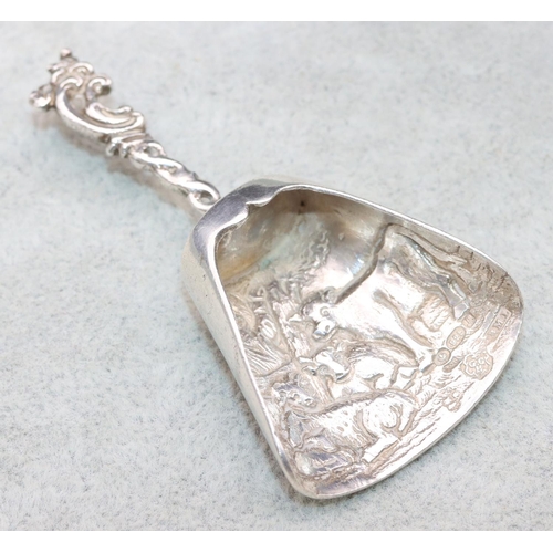 349 - An imported silver shovel shaped caddy spoon with embossed cattle and scroll decoration, 0.61oz