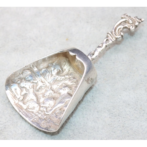 349 - An imported silver shovel shaped caddy spoon with embossed cattle and scroll decoration, 0.61oz