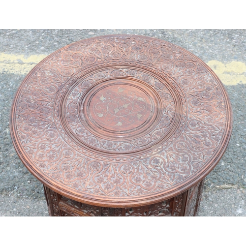 921 - An Eastern round hardwood coffee table with folding stand and allover carved and inlaid brass floral... 