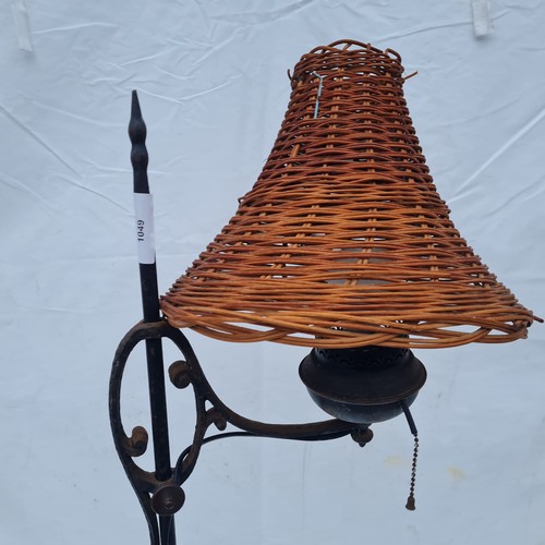 1049 - A wrought iron freestanding lamp with an interesting wicker lamp shade