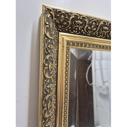 439 - A Bevelled edge wall hanging mirror in a heavily engraved Gold Gilt frame