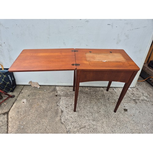 A mid century teak sewing table with extending platform