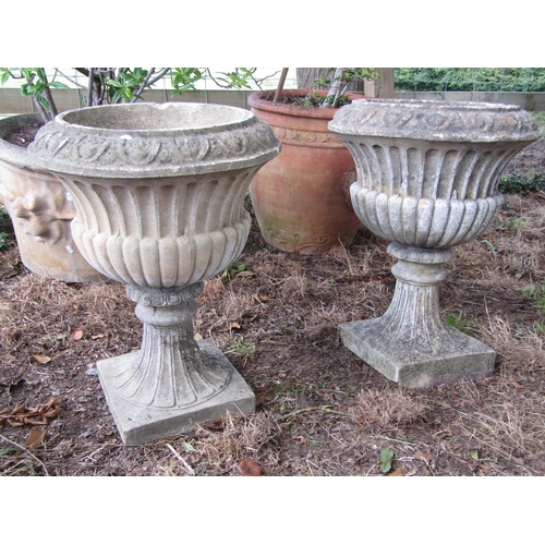 86 - A pair of reconstituted fluted urns on waisted stems and square cut bases, 60cm square