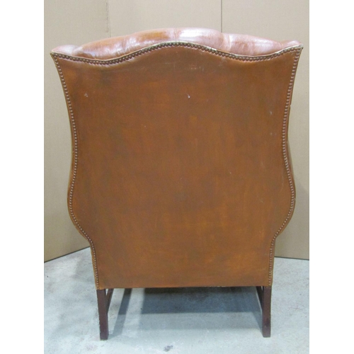 1919 - A Georgian style tan leather upholstered wing armchair, with button back, over a loose seat cushion,... 