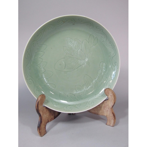 674 - An oriental celadon glazed dish of circular form, with incised fish and leaf detail with blue six ch... 