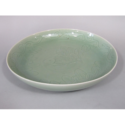 674 - An oriental celadon glazed dish of circular form, with incised fish and leaf detail with blue six ch... 