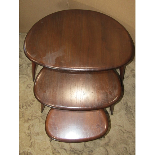 1951 - A nest of three Ercol dark stained elm and beechwood 'Pebble' occasional tables, raised on splayed s... 