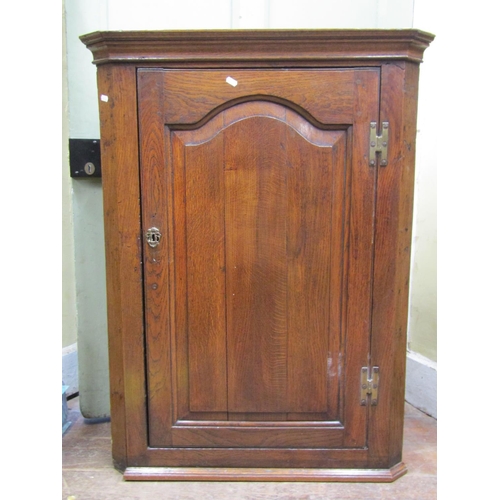 2665 - A Georgian oak hanging corner cupboard enclosed by an arched and fielded panelled door enclosing fou... 