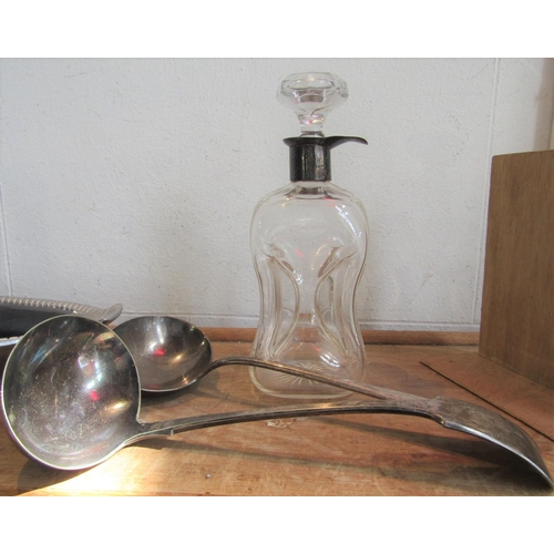 1214 - Silver coloured dimpled glass decanter, 24 cm high, together with two silver plated soup ladles (3)