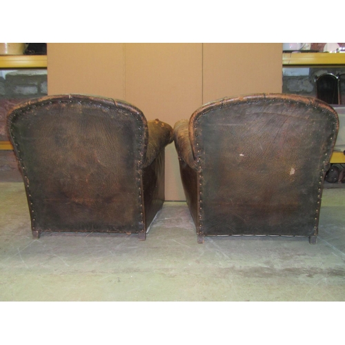 2325 - A pair of 1920/30's brown leather upholstered easy chairs with rolled arms,  button backs, loose sea... 