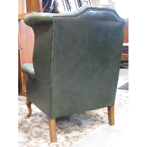 2257 - A reproduction Georgian style faux green leather upholstered wing armchair with button back, studded... 