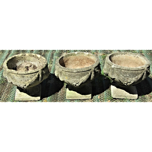 2080 - A set of three reclaimed garden urns, the circular bowls with repeating classical tied ribbon and sw... 