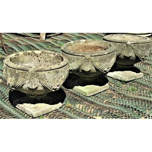 2080 - A set of three reclaimed garden urns, the circular bowls with repeating classical tied ribbon and sw... 