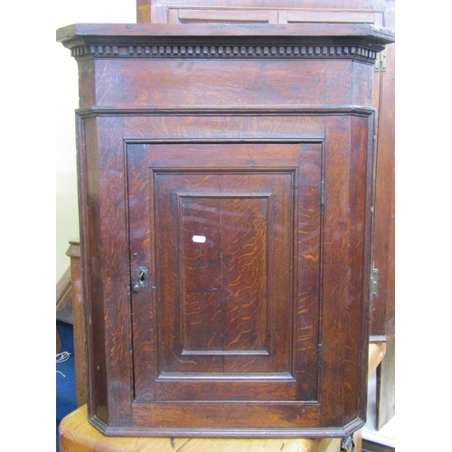 2766 - A small 18th century oak hanging  corner cupboard with panelled door and set beneath a dentil frieze... 