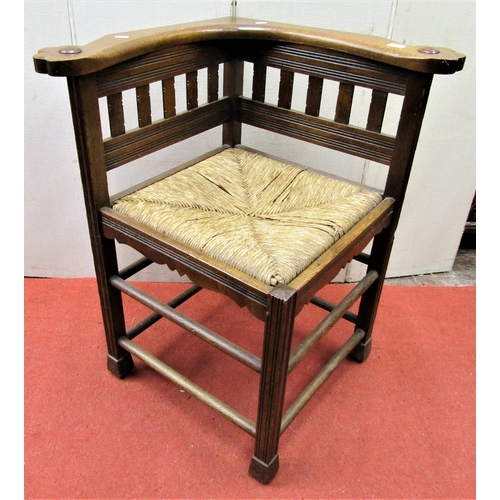 2752 - An Arts & Crafts period corner chair in oak with rush seat, reeded supports and further carved outli... 