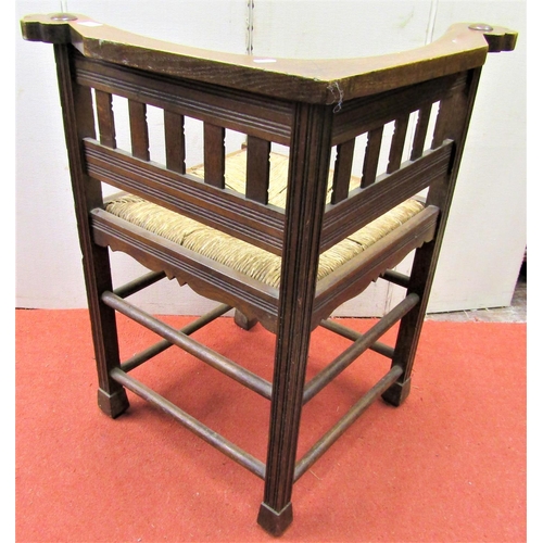 2752 - An Arts & Crafts period corner chair in oak with rush seat, reeded supports and further carved outli... 