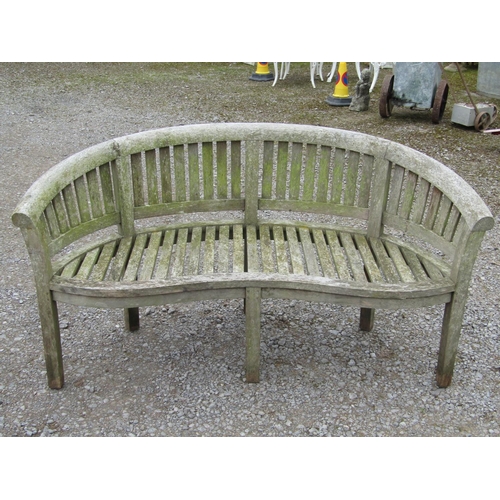 63 - A weathered teak banana shaped garden bench, 161cm long