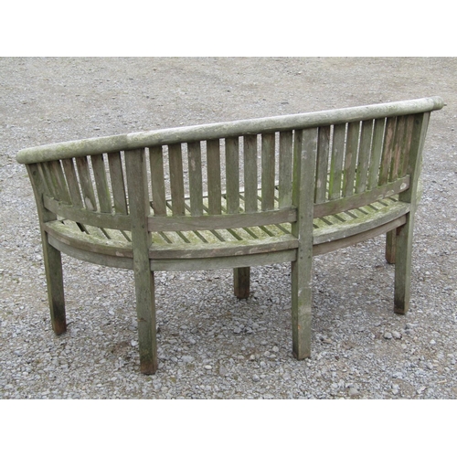 63 - A weathered teak banana shaped garden bench, 161cm long