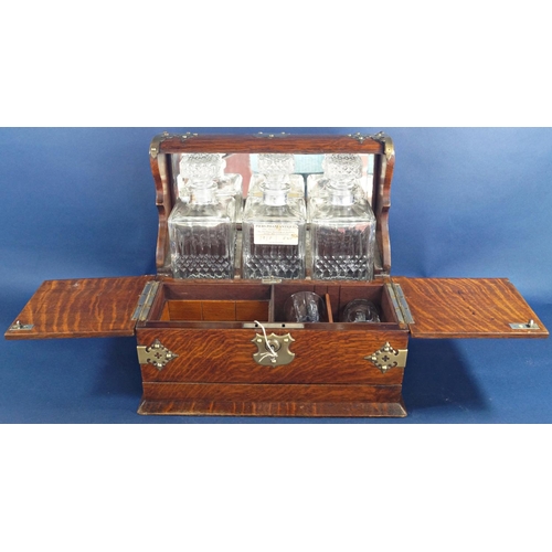 1136 - A Victorian oak games tantalus with brass overlay, having three matching decanters and two glasses, ... 