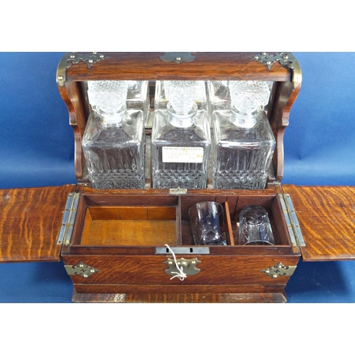 1136 - A Victorian oak games tantalus with brass overlay, having three matching decanters and two glasses, ... 