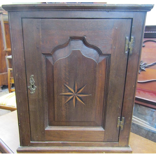 2446 - An 18th century oak hanging wall cupboard enclosed by a shaped and fielded panel with marquetry star... 