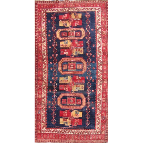 2467 - A Middle Eastern corridor rug, with a central row of gul and elephant foot medallions on a blue grou... 