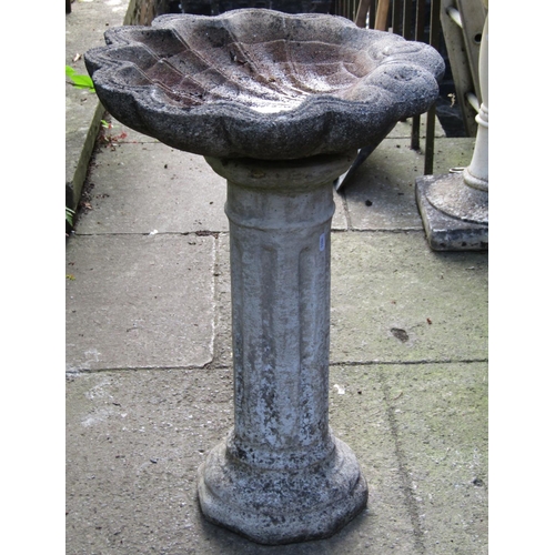 1073 - A weathered cast composition stone bird bath, the scallop shell shaped bowl raised on a fluted pedes... 