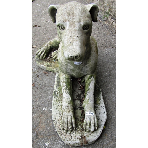 1129 - A weathered cast composition stone garden ornament in the form of a recumbent greyhound set on a sha... 