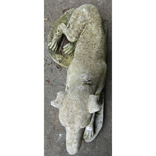 1129 - A weathered cast composition stone garden ornament in the form of a recumbent greyhound set on a sha... 