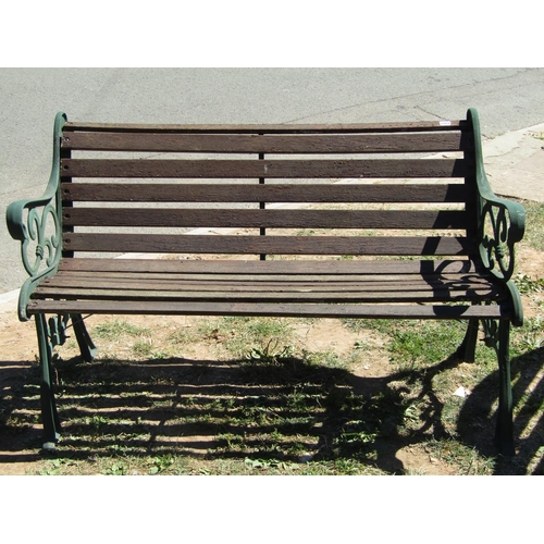 1084 - A two seat garden bench with weathered hardwood lathes, raised on green painted decorative cast iron... 